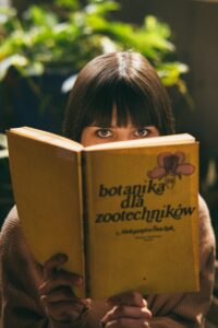 Książka testowa A young woman with bangs reads a botanical book indoors, creating a warm and focused ambiance.